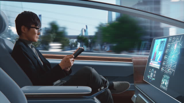 Futuristic Concept: Handsome Stylish Japanese Businessman in Glasses Reading Notebook and Watching News on Augmented Reality Screen while Sitting in a Autonomous Self-Driving Zero-Emissions Car.
