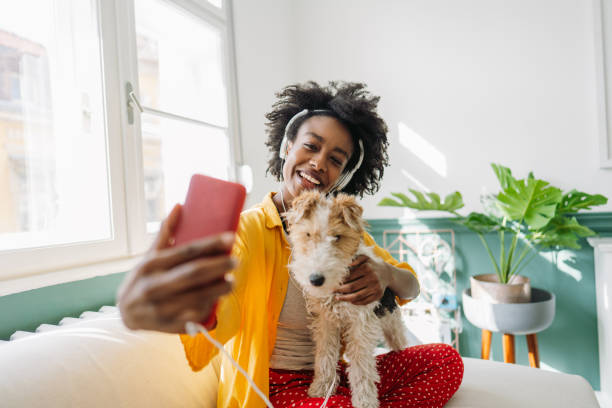 Young woman and her dog on a video call Photo of a young smiling woman of African American ethnicity, using mobile phone and talking with a friend on video call, while holding and embracing her dog arab culture photos stock pictures, royalty-free photos & images