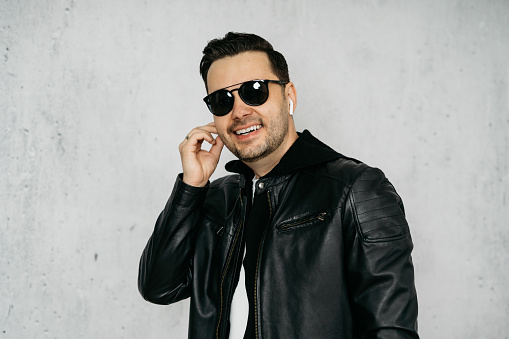 Man wearing wireless in-ear headphones, a black leather jacket and sunglasses