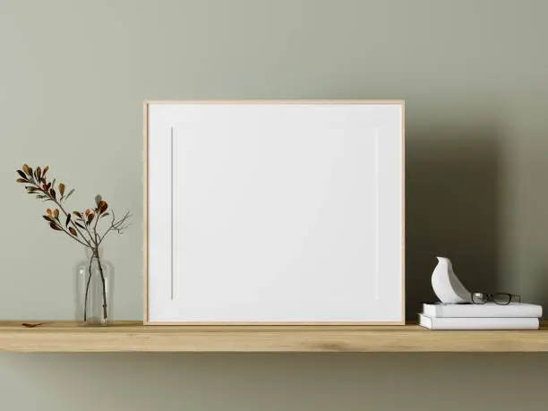Photo of Empty white mock up picture frame on wooden shelf with green plant decoration