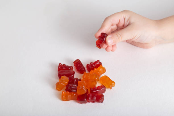 istock Small child's hand holds multicolored kids vitamins teddy bear on white background, isolate. Multivitamins 1317614142
