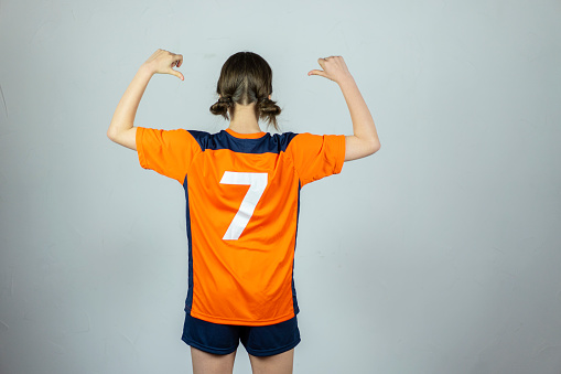 Full-length portrait of sportive girl, female soccer, football player posing isolated on white studio background. Concept of sport, fitness, women in sports. Young sportive wearing football kit.