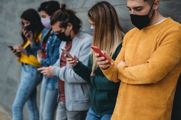 Side view of people using smart phones against a wall Side view of people using smart phones against a wall. They are surfing the net and sharing content. They are wearing protective face masks. fake news stock pictures, royalty-free photos & images