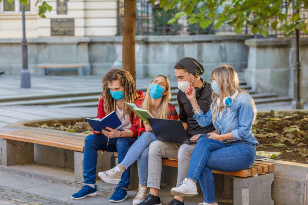 istock Beautiful Students are Working on a Laptop in Public Park with Preventive Measures due to Coronavirus. 1317615820