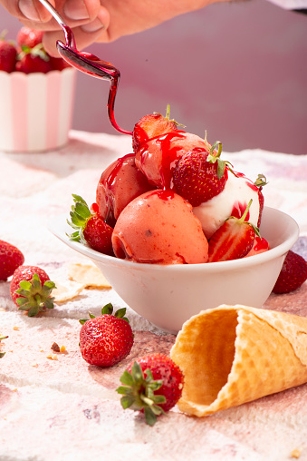 a hand is putting down shouroup with spoon to strawberry icecream food styling for social media food trend photo