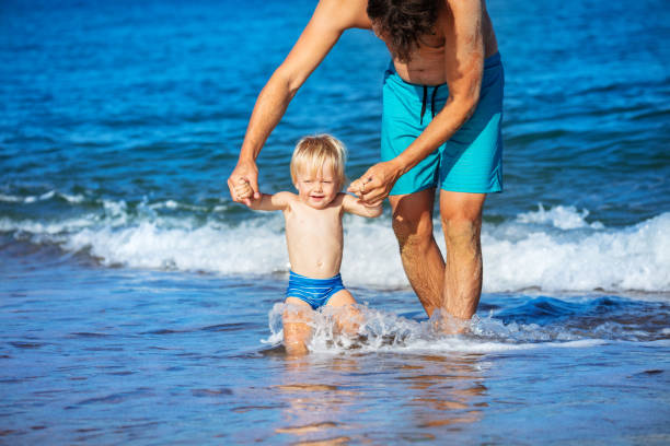 istock Father walk toddler boy hold hands in sea waves 1317617149