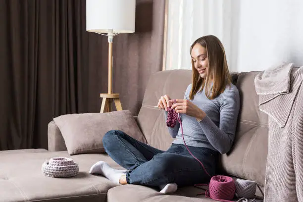 Young woman is relaxing at evening at home,  knits sitting on a sofa.