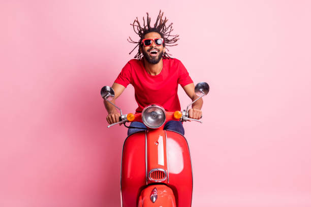 Portrait of handsome cheery dreamy guy riding moped having fun wind blowing spending summer isolated over pink pastel color background