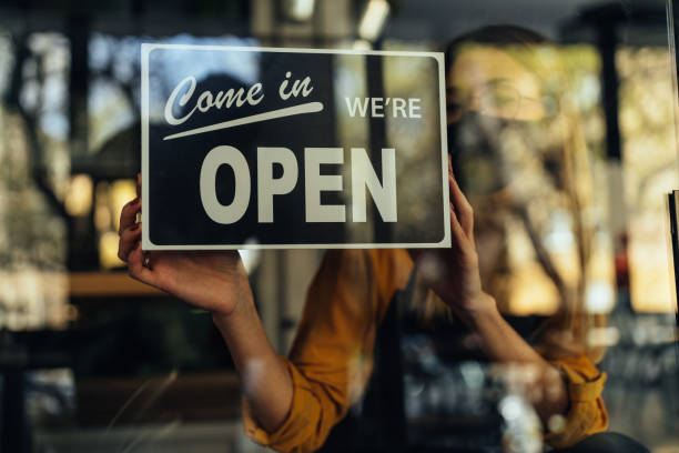 istock Young entrepreneur with face mask posting Open sign on front door 1317622424