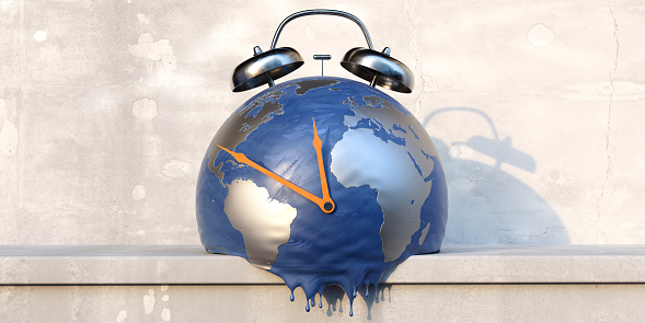 A render of an abstracted deflated and melting earth globe with silver metallic land masses and blue 'sea' with orange painted clock hands and silver alarm bells. The clock is sitting on a concrete shelf against a worn concrete wall.