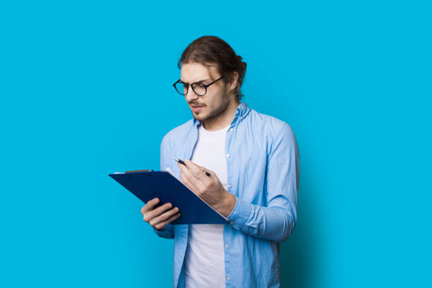 istock Young concentrated man with beard and long hair with glasses is planning something on a map posing on a blue studio wall 1317623773