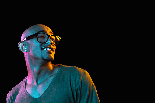 Cheerful. African-american young man's portrait on dark studio background in neon light. Beautiful male model in casual style. Concept of human emotions, facial expression, youth, sales, ad.