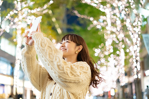 Asian (Japanese) young woman shooting illuminations that color the city at night with a smartphone