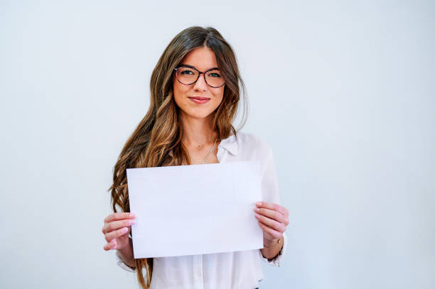 disparo de una atractiva joven empresaria de pie sola contra una pared blanca y sosteniendo una pancarta en blanco - businesswoman advertise placard advertisement fotografías e imágenes de stock