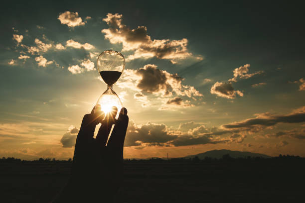 istock hand holding hourglass at sunset time. 1317628355
