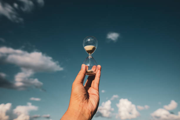 istock hand holding hourglass at sunset time. 1317628356
