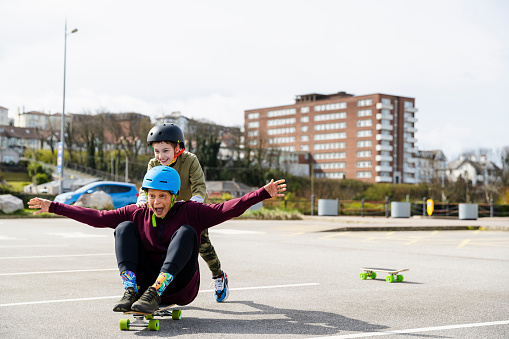 Mid age woman and her son skateboarding in a parking lot in Liverpool in the North of England. The son is pushing his mother who is sitting on the board.