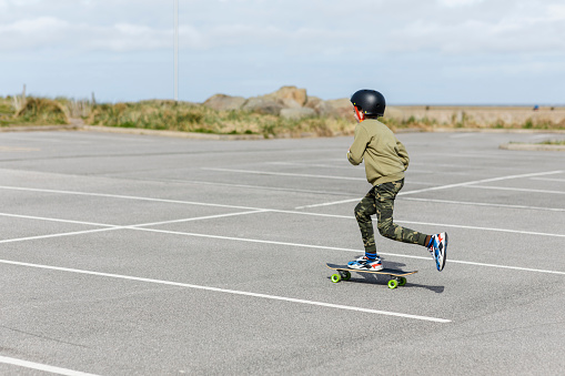 Side view of a boy skateboarding in a parking lot in Liverpool in the North of England. He is sitting on the board pushing himself along.