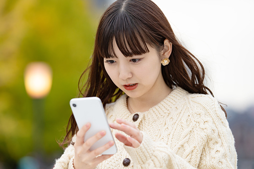 Asian (Japanese) young woman operating a smartphone with an uneasy look
