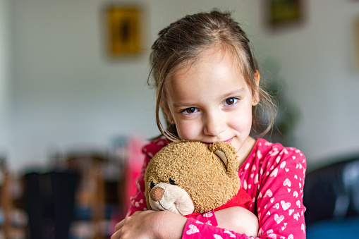 Cute little girl embracing her teddy bear indoors