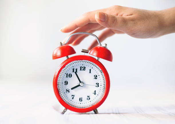 istock Time optimization concept. Female hand holding alarm clock on bed background, close up view 1317633086