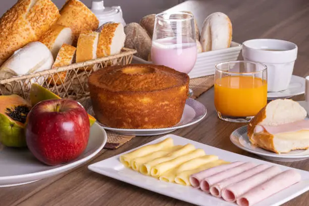 Breakfast table filled with various foods including breads, sweets, cake, yogurt, tea, coffee, orange juice, ham, cheese, papaya and apple