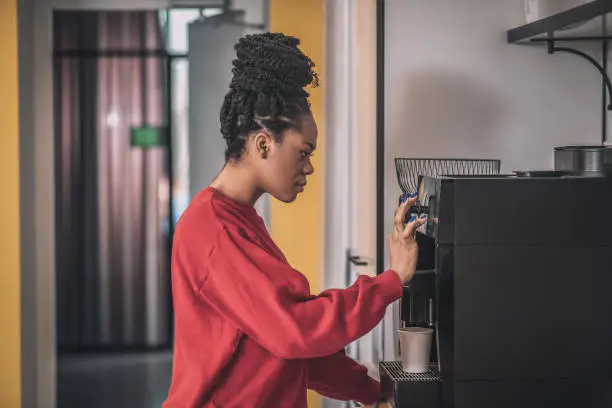 Coffee break. Dark-skinned young woman standing near the coffee-machine