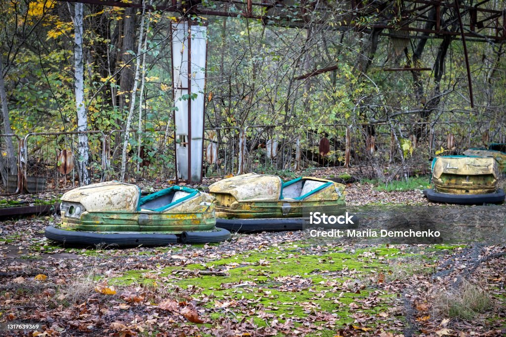 Old broken abandoned rusty metal radioactive yellow cars among moss and autumn leaves in amusement park in ghost town Pripyat, Chernobyl Exclusion Zone Old broken abandoned rusty metal radioactive yellow cars among moss and autumn leaves in amusement park in ghost town Pripyat, Chernobyl Exclusion Zone. Tilt-shift effect Pripyat City Stock Photo