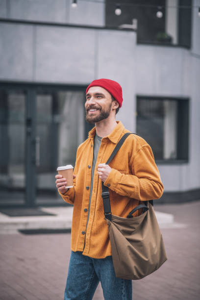 istock Man in a red hat and orange jacket with a coffee cup in hands 1317639960