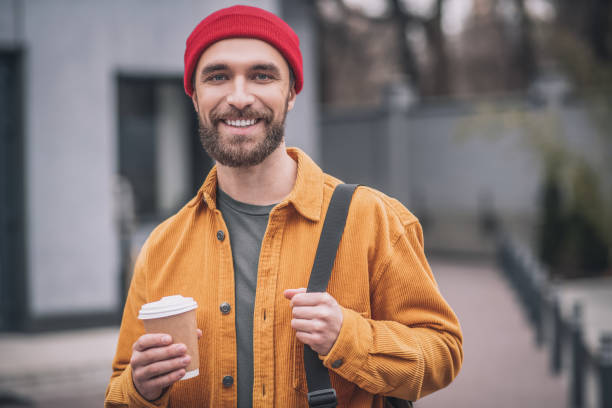 istock Man in a red hat and orange jacket with a coffee cup in hands 1317639963