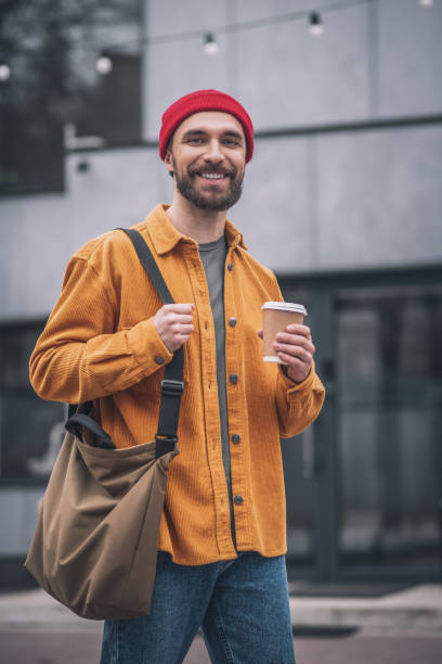 istock Man in a red hat and orange jacket with a coffee cup in hands 1317639970