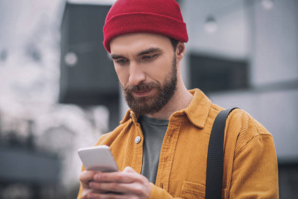 istock Man in a red hat holding his phone and texting a message 1317640034