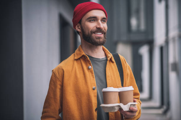 istock Young bearded man in a red hat holding coffee cups 1317640066