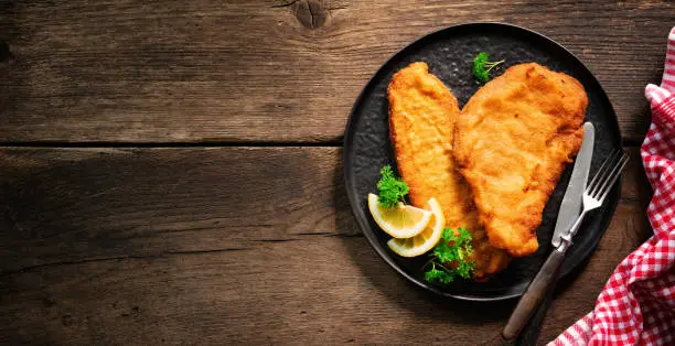 Homemade breaded wiener schnitzel served with parsley and lemon slices on dark wooden table