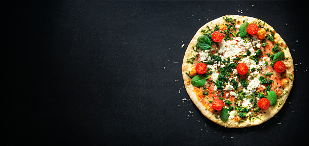 Crispy spinach pizza with ricotta, mozzarella and tomatoes on dark background. Healthy nutrition vegan lifestyle. Italian cuisine for vegetarians