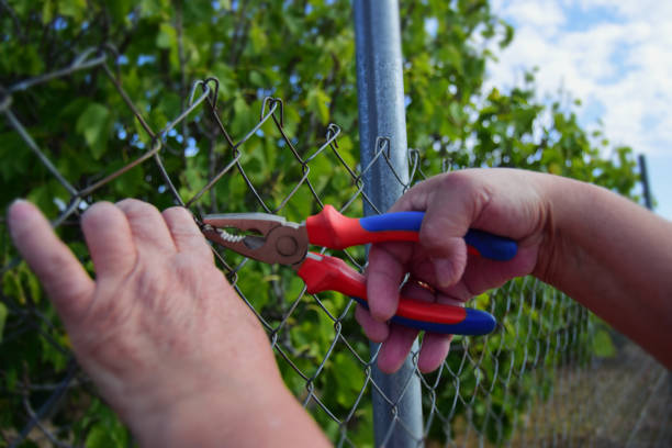 Woman's hands working on a wire fence and metal gate