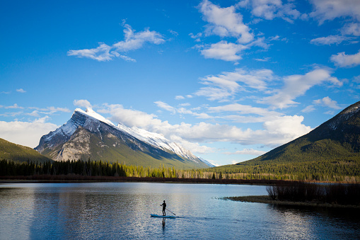 A woman goes for a stand-up paddleboard adventure on Vermillion Lakes in Banff National Park, Alberta, Canada. The snowcapped Mt. Rundle above the town of Banff is in the background.