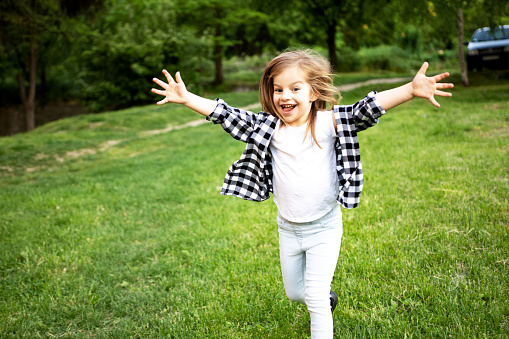 Happy Little girl running with open arms in the park nature
