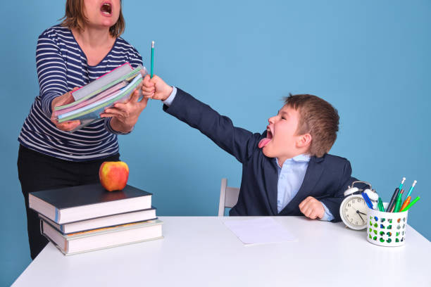 niño con uniforme escolar pelea con mamá por lecciones sobre fondo azul - furious blue little boys caucasian fotografías e imágenes de stock