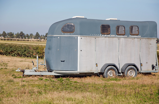 A horse trailer with graphics is ready to hook up and go . silver horse trailer on green weadow . A trailer used for transporting one adult horse A trailer used for transporting one adult horse.