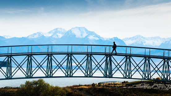 Tourist walking on the footbridge with mighty Southern Alps in the background, Lake Tekapo, South Island