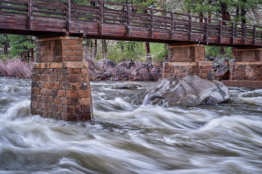 Poudre River under Greyrock trail bridge in a canyon above Fort Collins, Colorado, rainy spring scenery with high flow