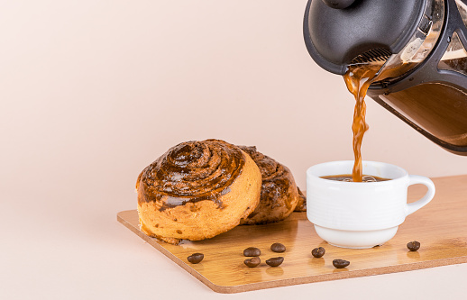 Pouring black coffee into a white cup. Two freshly baked cinnamon rolls. Copy space.