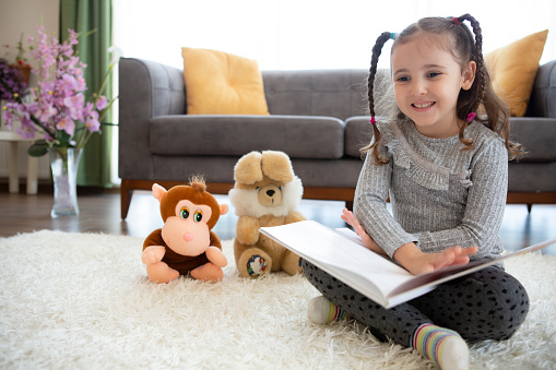 Cute little girl playing alone reading book to toy