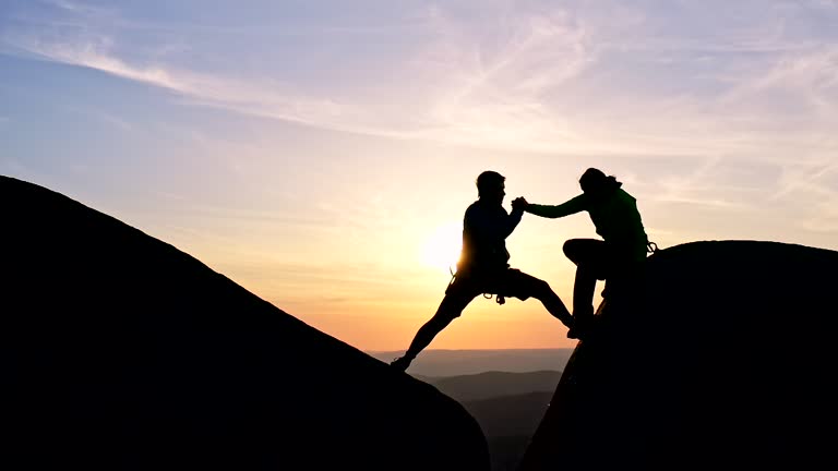 Slow motion of a man gives a hand to a woman helping her down a cliff face.