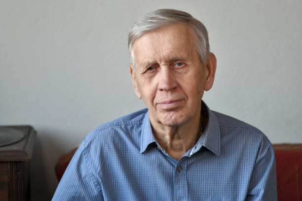 portrait of a cute 80 year old man sitting on the sofa at home. - 80 year old imagens e fotografias de stock