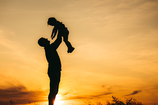 Father throwing his daughter in the air at sunset.