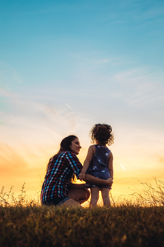 Mother and daughter embracing at sunset on a meadow.