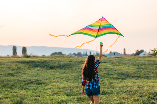 Happy young woman running with a kite on a meadow at sunset in summer.