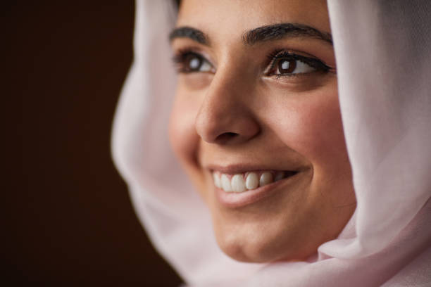 Extreme close up of young Middle-Eastern woman wearing veil and smiling cheerfully looking away while posing in studio, copy space